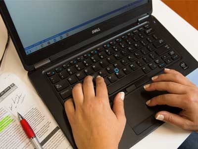 Pen, notes and an open laptop showing hands writing on the keyboard