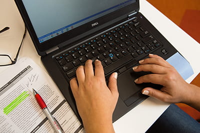 Hands on laptop keyboard with pen and paper alongside