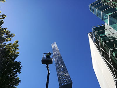 View of staff member in a cherry picker cleaning the upper part of the Chevron sculpture.