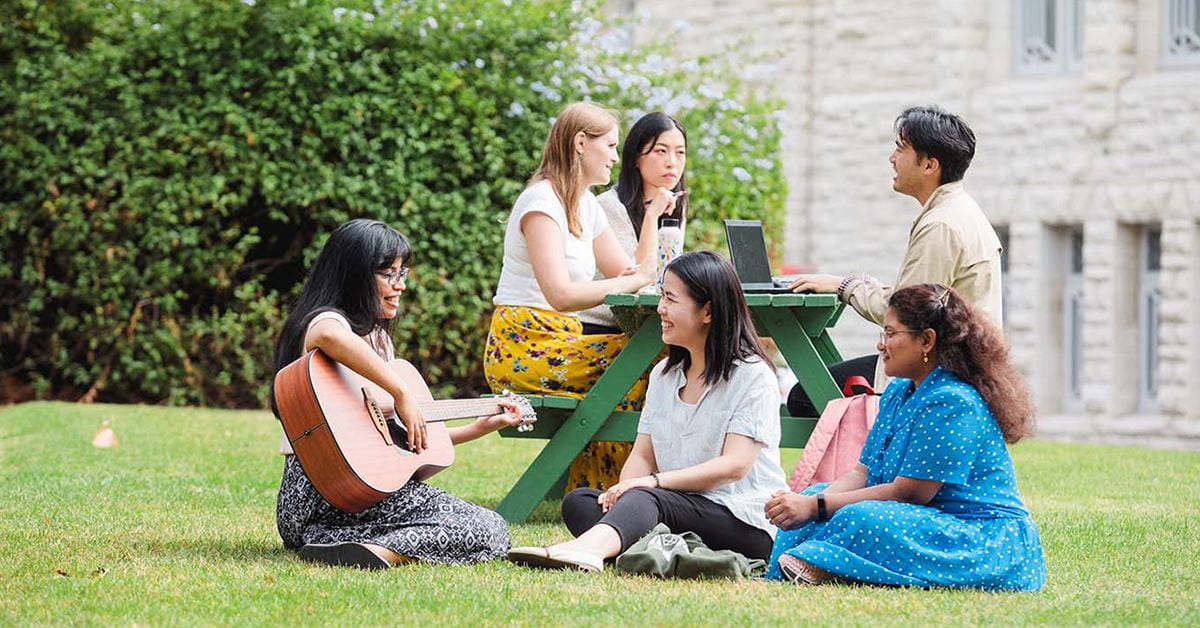 Students smiling sitting outdoors on University of Auckland grounds