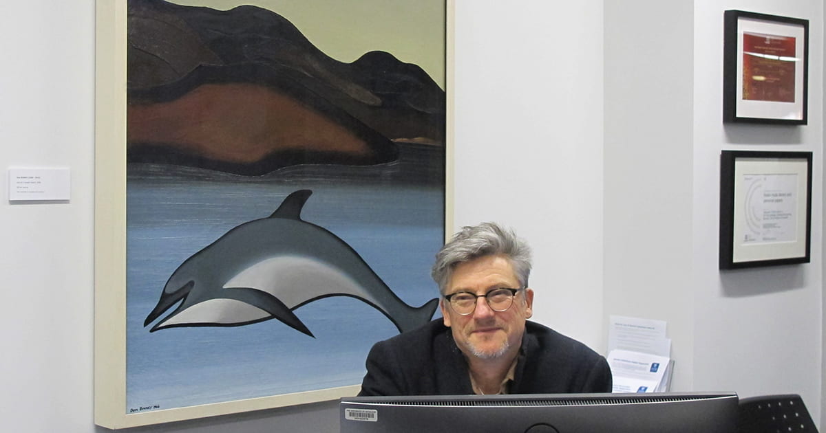 Nigel Bond, Team Leader, Cultural Collections, sits in front of Don Binney's 'In the Lee of a Looted Island' (1966).