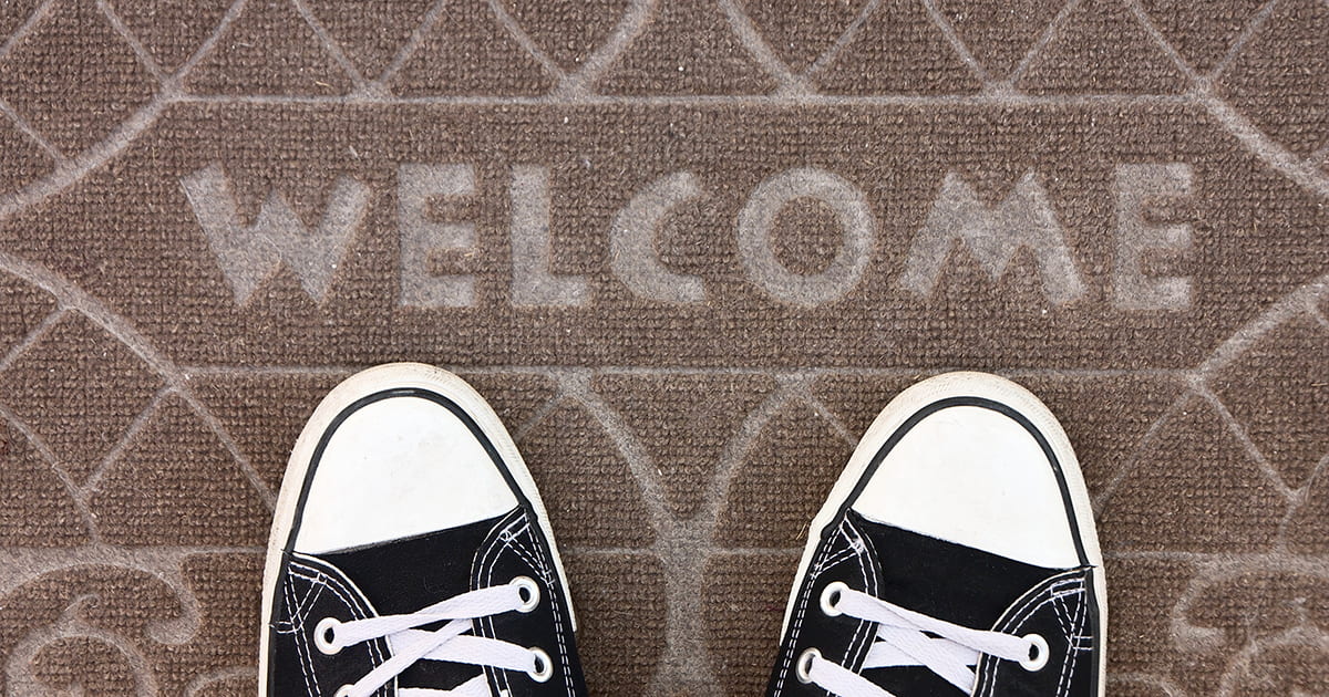 Doormat with 'Welcome' written on it and a pair of feet standing on it.